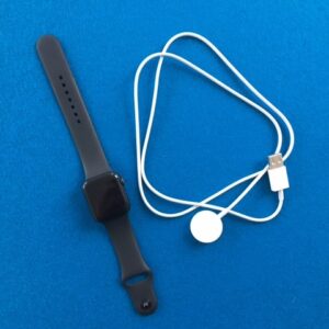 Auf einer dunkelblauen Filzunterlage liegt links die Apple Watch Series 6. Sie ist schwarz. Links daneben liegt das magnetische Ladkabel der Apple Watch. Es ist weiß.